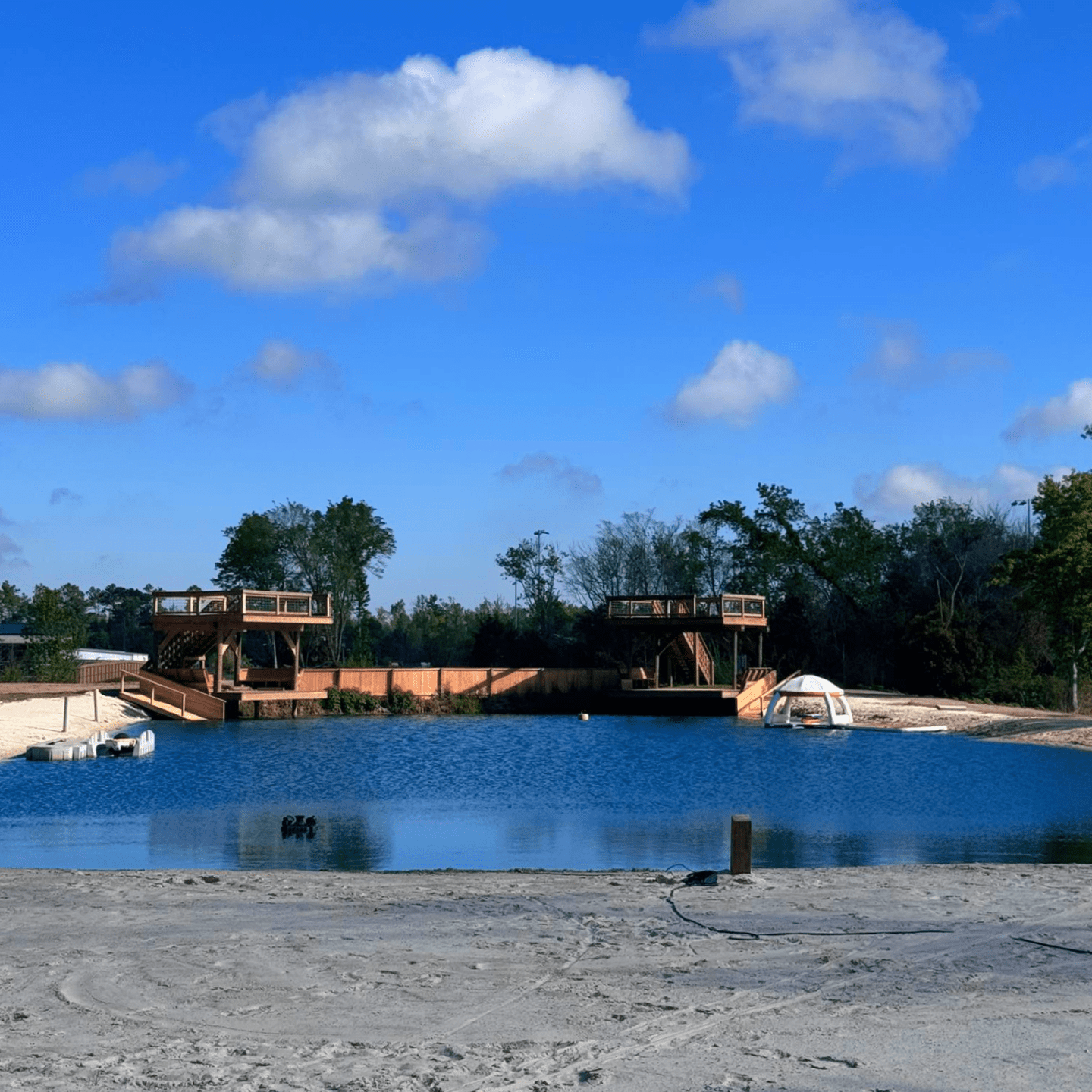 Sandy beach by a lake with wooden platforms and trees under a blue sky.