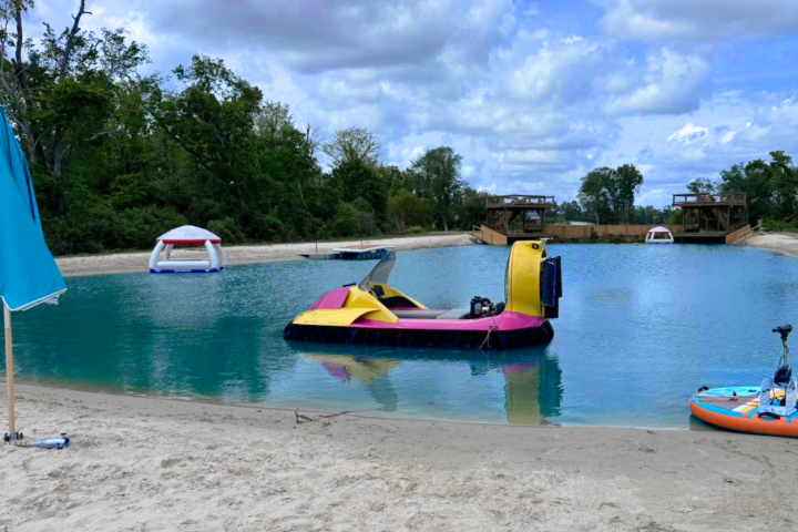 Sandy beach with colorful pedal boats on a pond, under a cloudy sky.