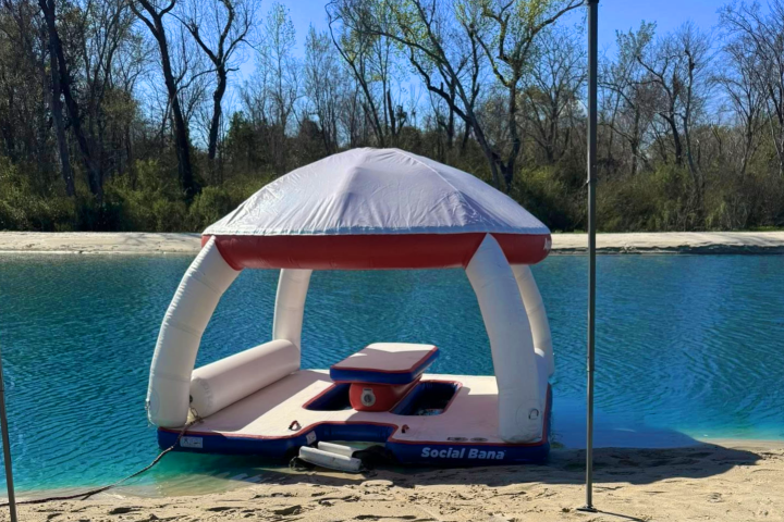 Inflatable raft with canopy on a lake shore, surrounded by trees.