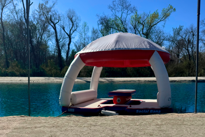 Floating platform with a canopy on a lake near trees.