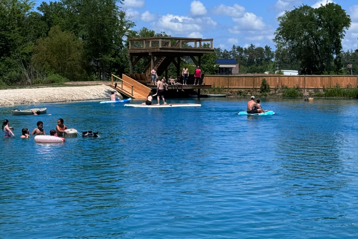 People swimming and relaxing by a lake with a waterslide and dock.