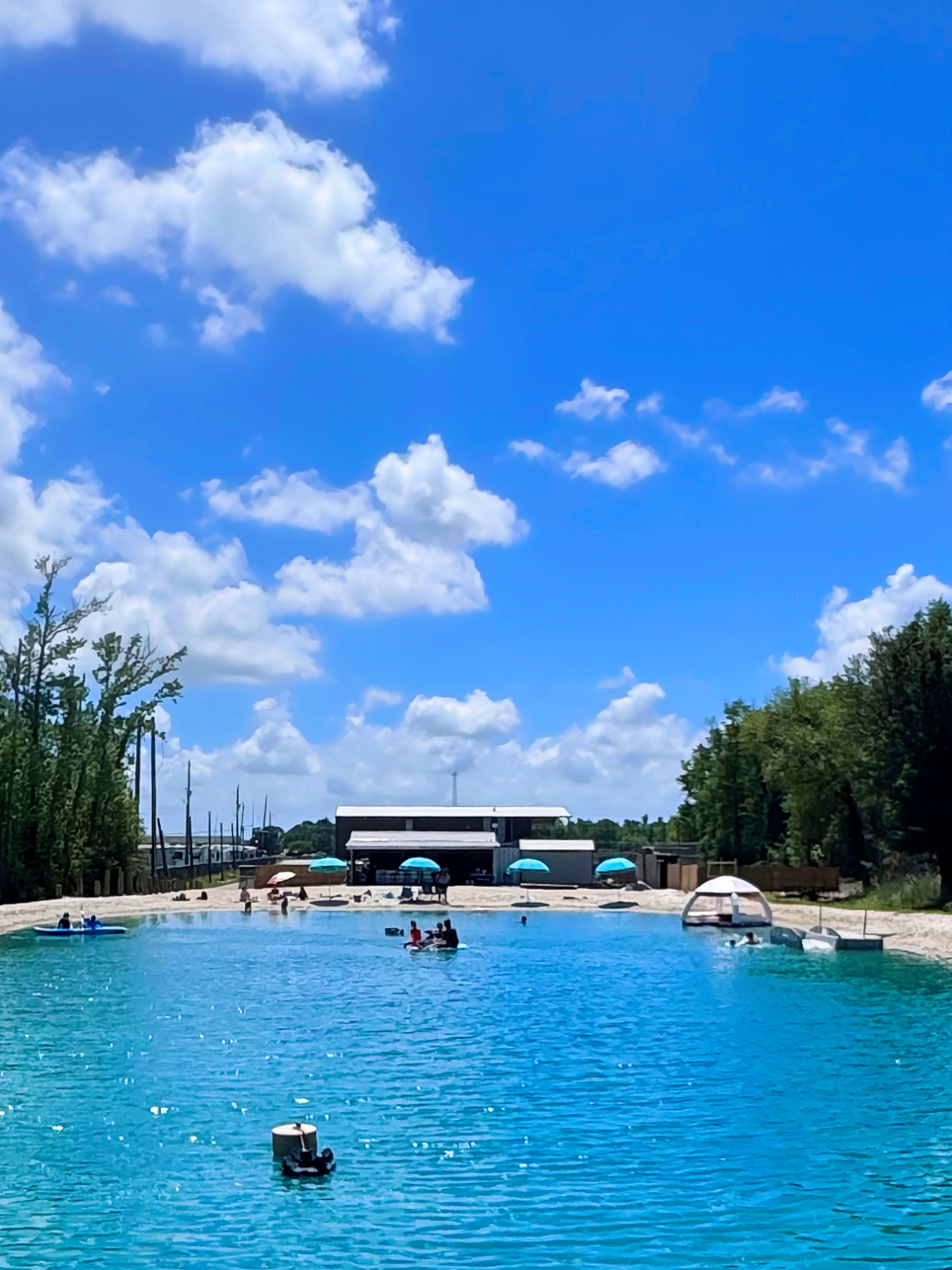 People relaxing by a turquoise lagoon under a partly cloudy blue sky.