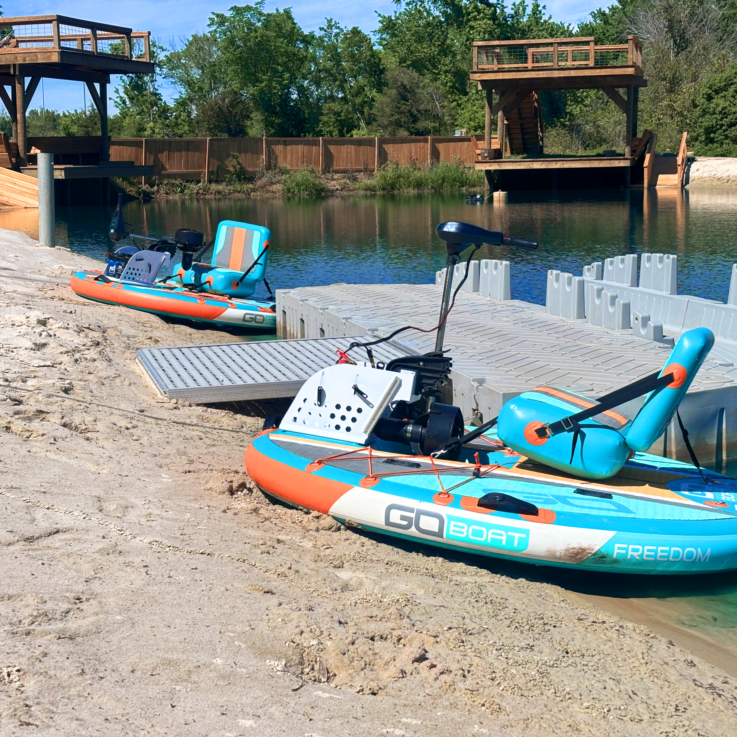 Two orange and blue small boats docked on sandy shore with wooden structures in the background.