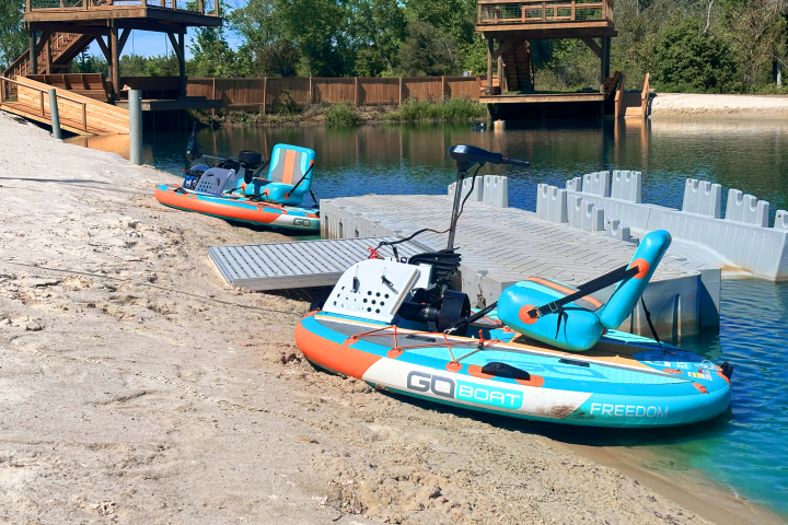 Two orange and blue small boats docked on sandy shore with wooden structures in the background.