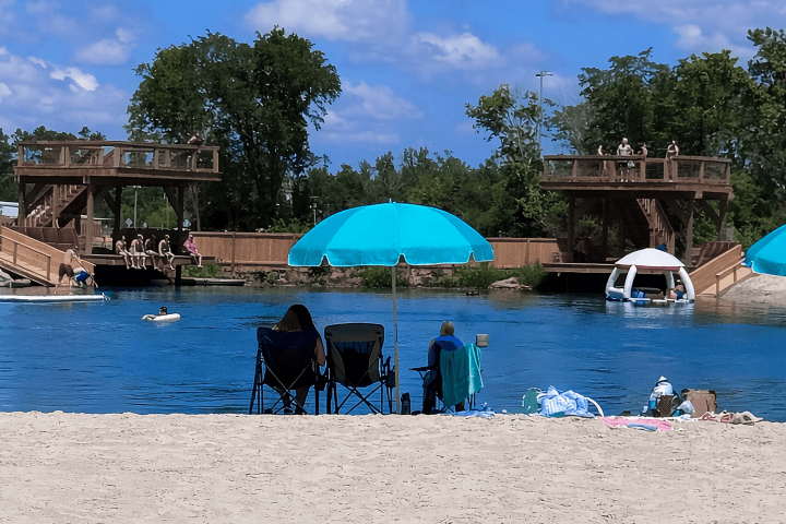 Beach scene with chairs, umbrellas, and people near water.