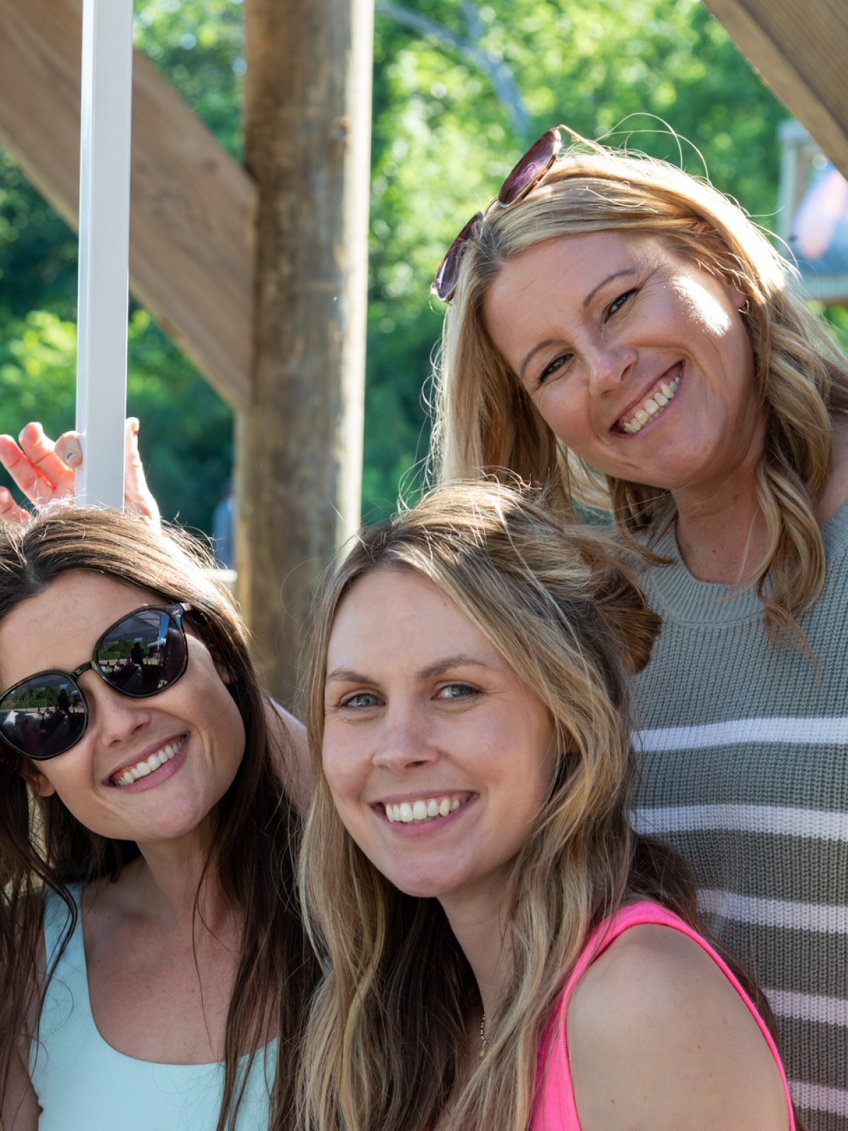 Three women smiling outdoors near a pool with greenery in the background.