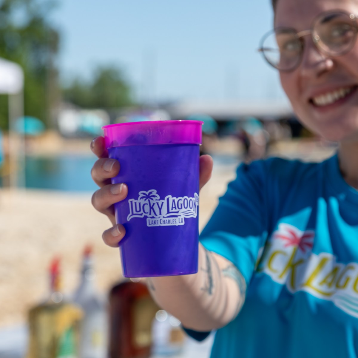 Person smiling, holding a purple Lucky Lagoon cup at an outdoor event.