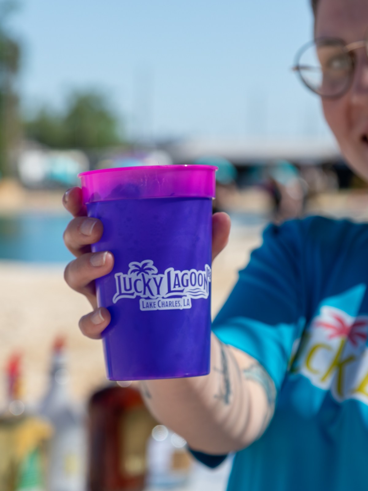 Person smiling, holding a purple Lucky Lagoon cup at an outdoor event.