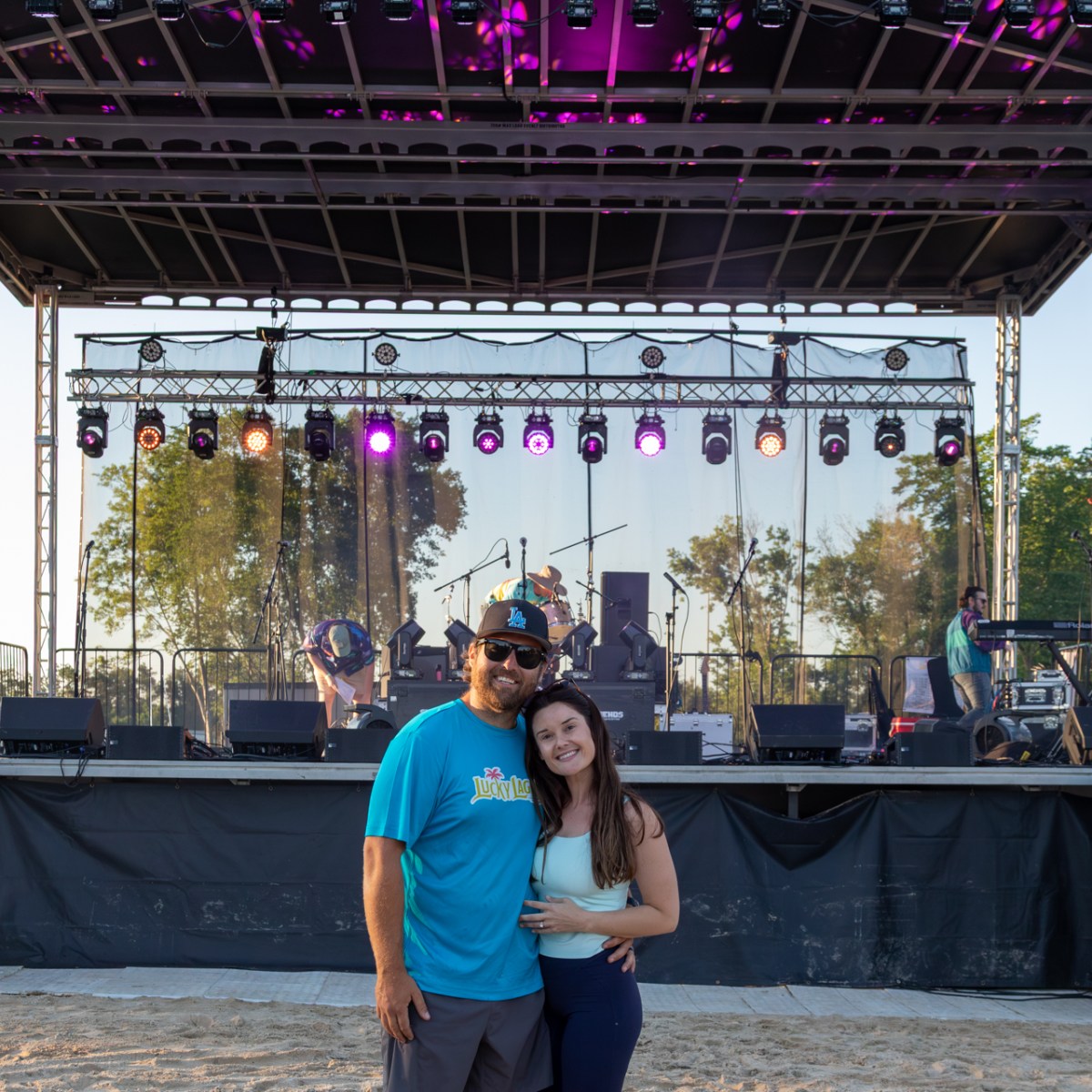Couple posing on sandy ground in front of stage with 'Lucky Lagoon' sign.