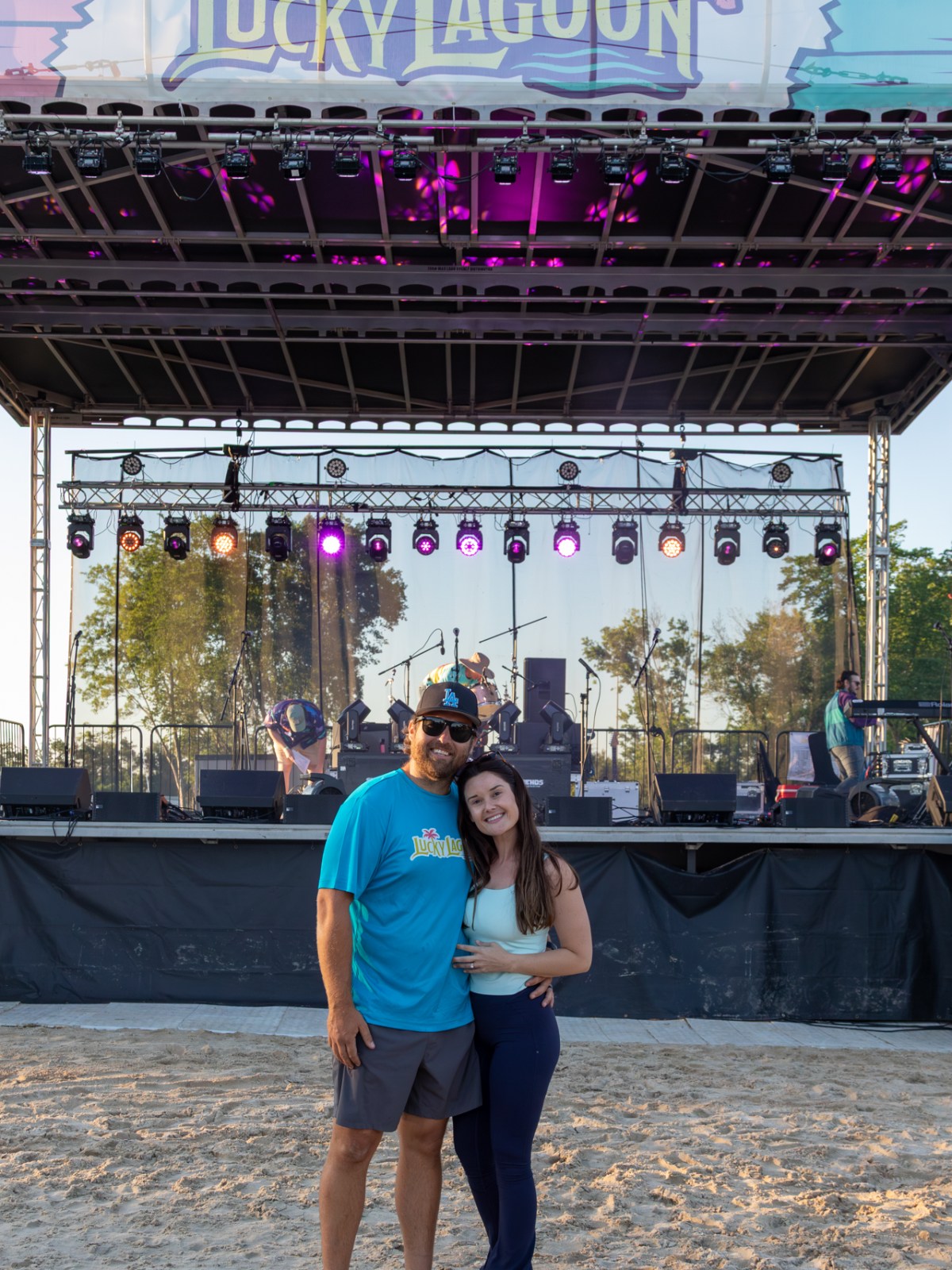 Couple posing on sandy ground in front of stage with 'Lucky Lagoon' sign.