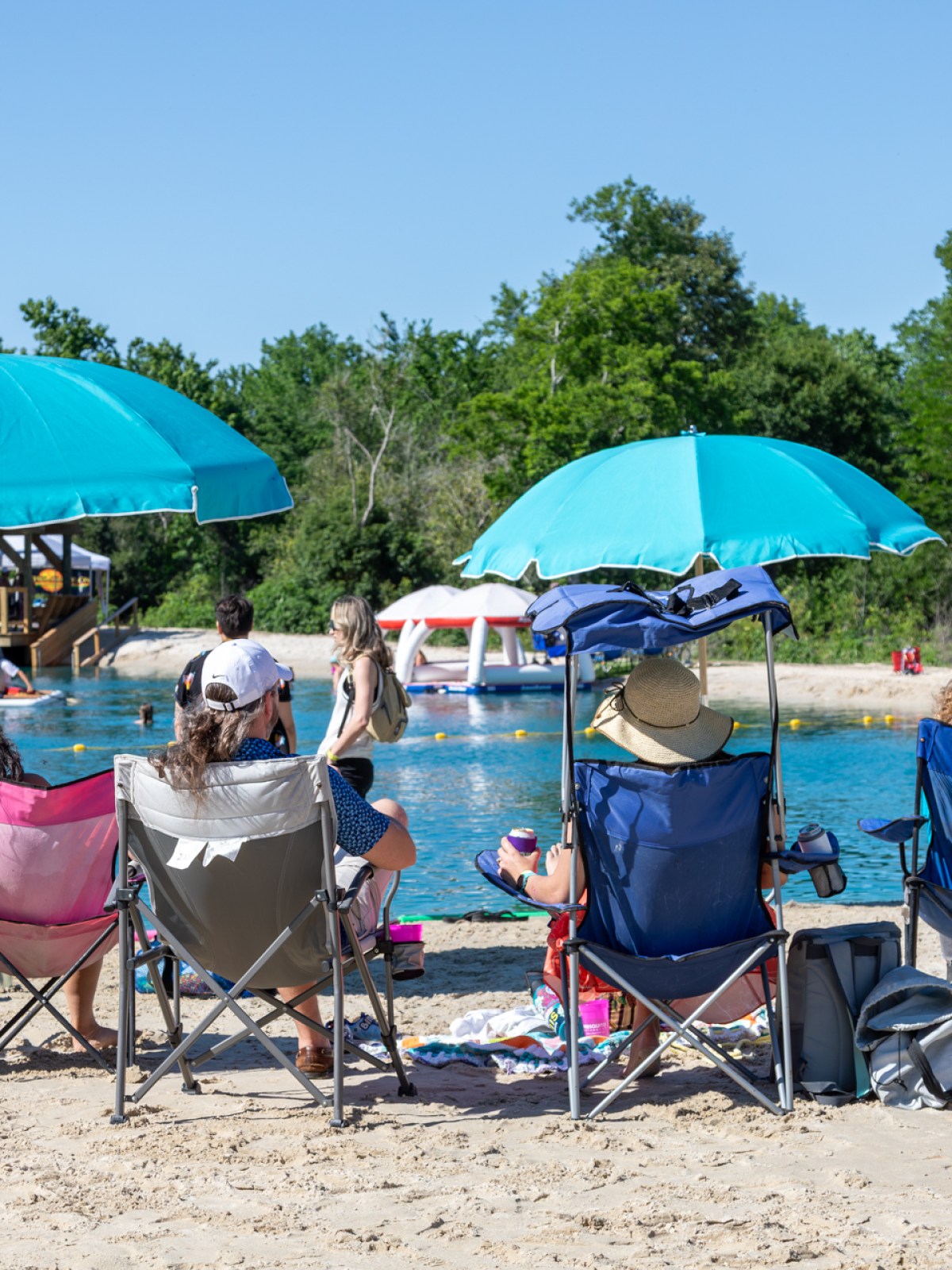 People on beach chairs under umbrellas by a lake.