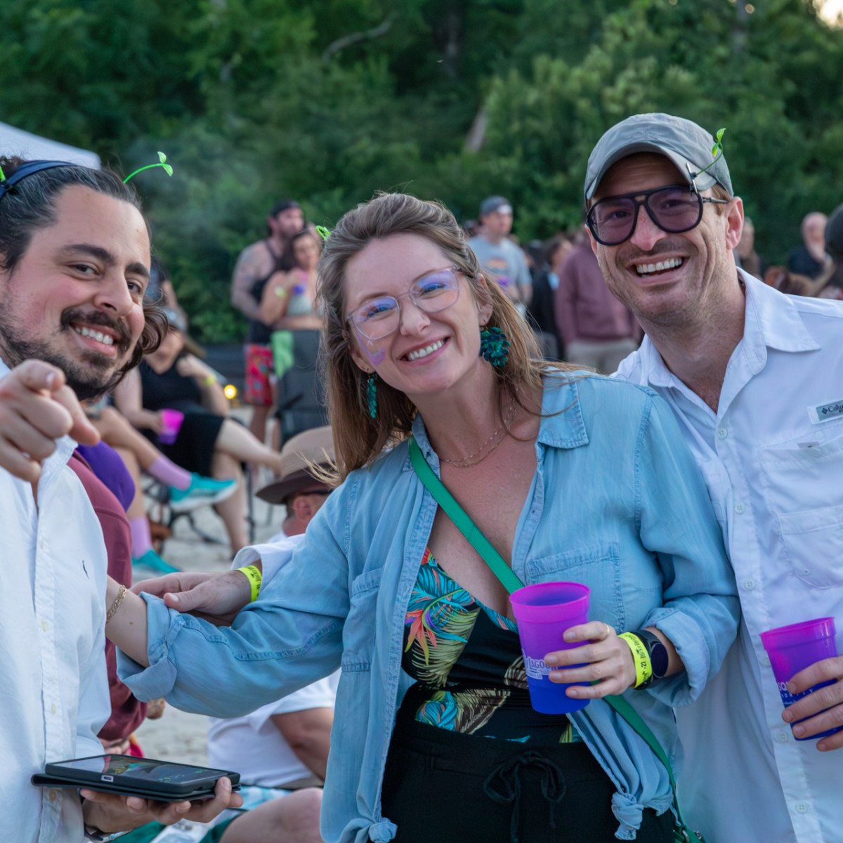 Three people at an outdoor event, smiling and holding drinks.