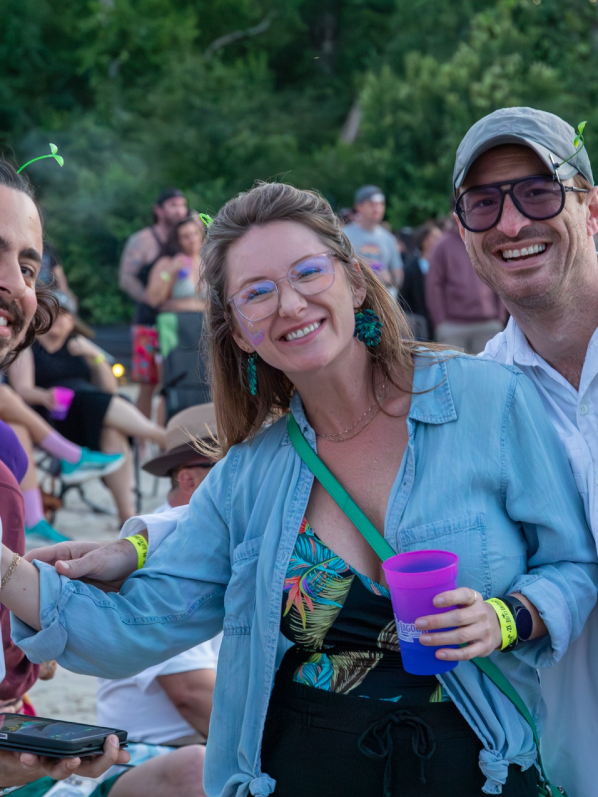 Three people at an outdoor event, smiling and holding drinks.